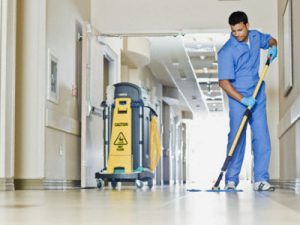 Hospital cleaning in progress by a cleaning professional in sanitary work clothes.