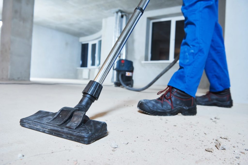 A uniformed man uses a heavy duty vacuum to complete construction cleanup.